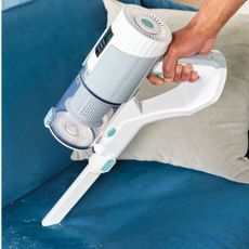 Using the white Aldi cordless vacuum to clean up crumsb on a blue sofa