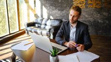 A business owner looks at his laptop at his desk in his office. 