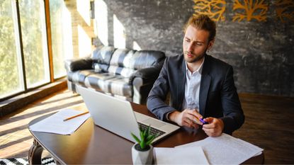A business owner looks at his laptop at his desk in his office. 