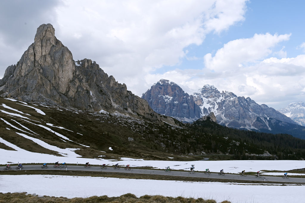 A wide shot of the Passo Giau, with Dolomites mountains in the backgrounds and cyclists on the road in the foreground