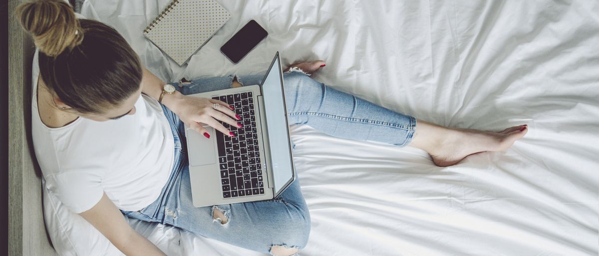 Coursera review 2021: Image shows young woman on bed studying with laptop and notepad