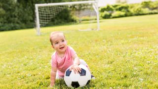 baby girl playing on grass with football - stock photo
