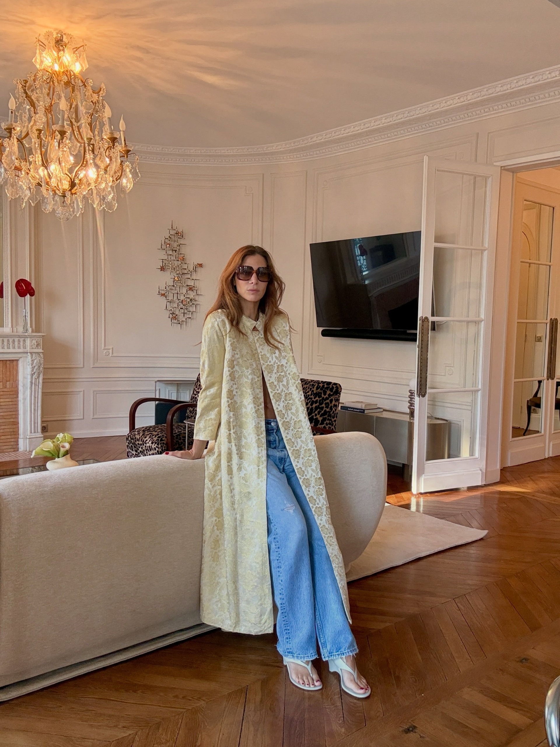 An image of @jen_wonders wearing an ornate coat with blue jeans and white wedge heels.