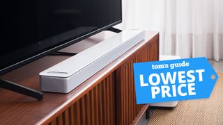 Bose Smart Soundbar 900 in white in front of a TV set with lowest price deal tag