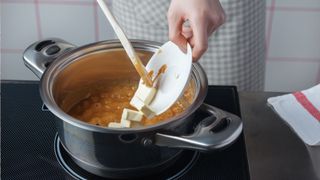 A person adding butter to caramel in a pan