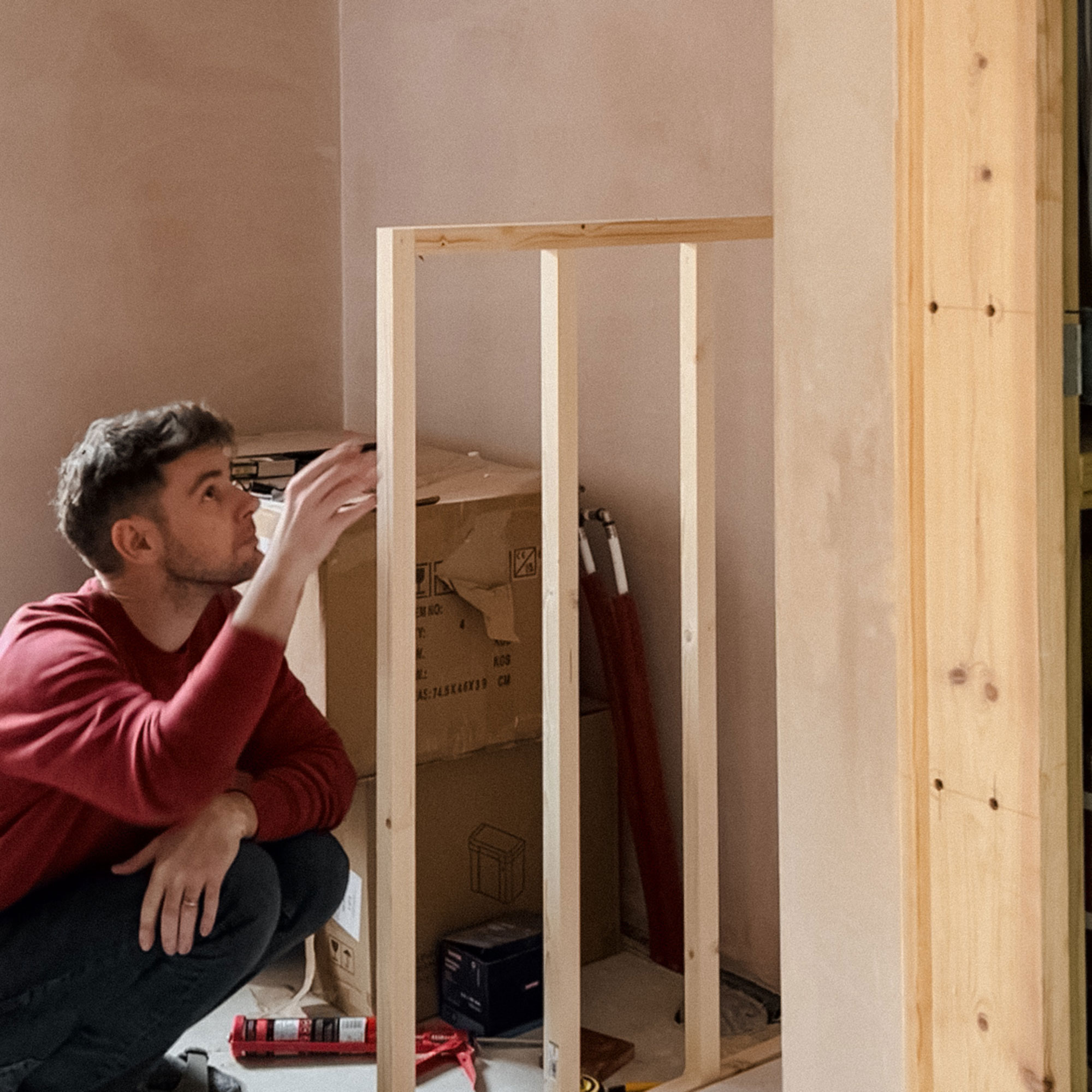 Man crouching looking at stud half-height wall in room mid-renovation