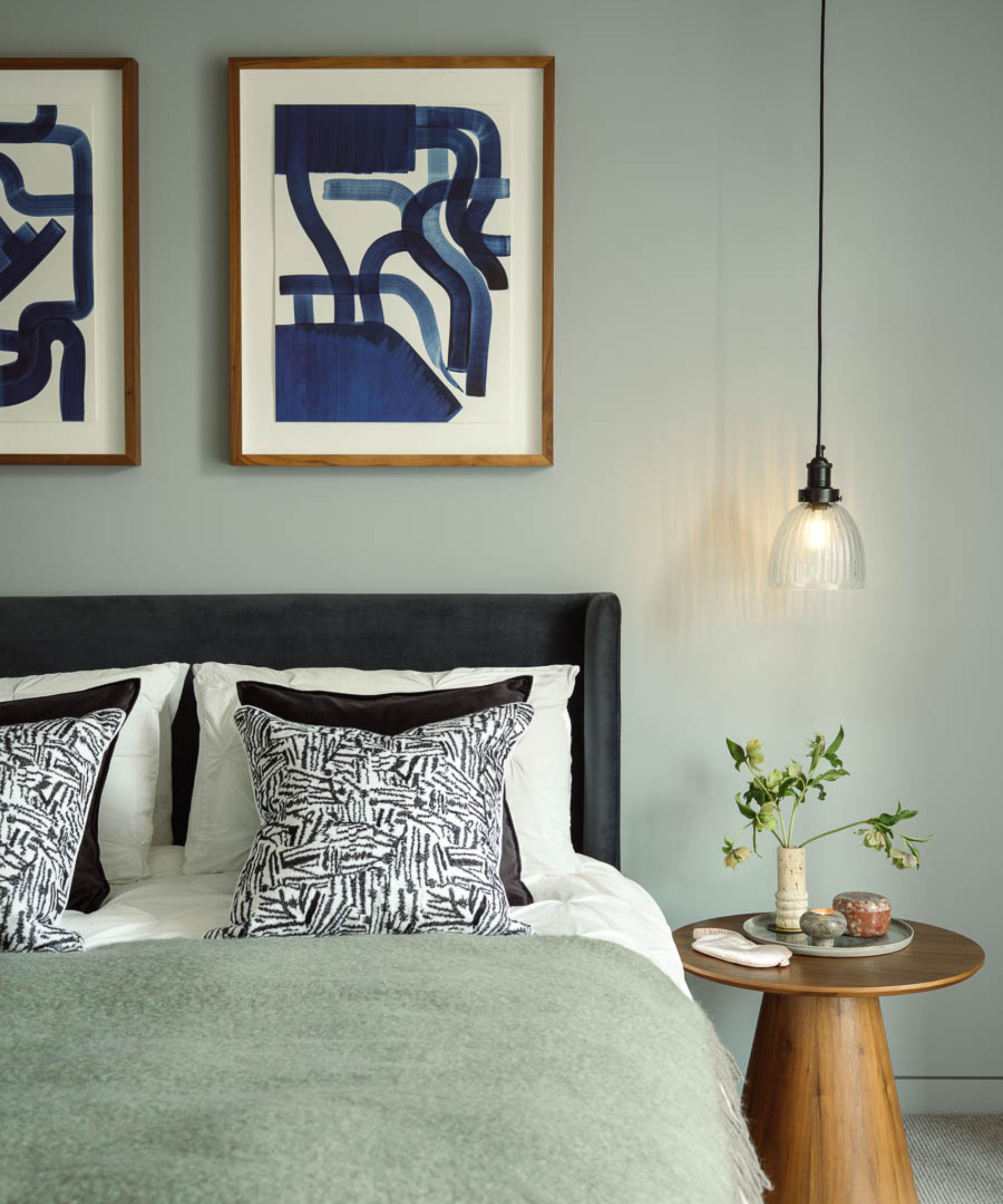 Sage green bedroom with abstract wall art, double bed with sage wool throw and wood round side table