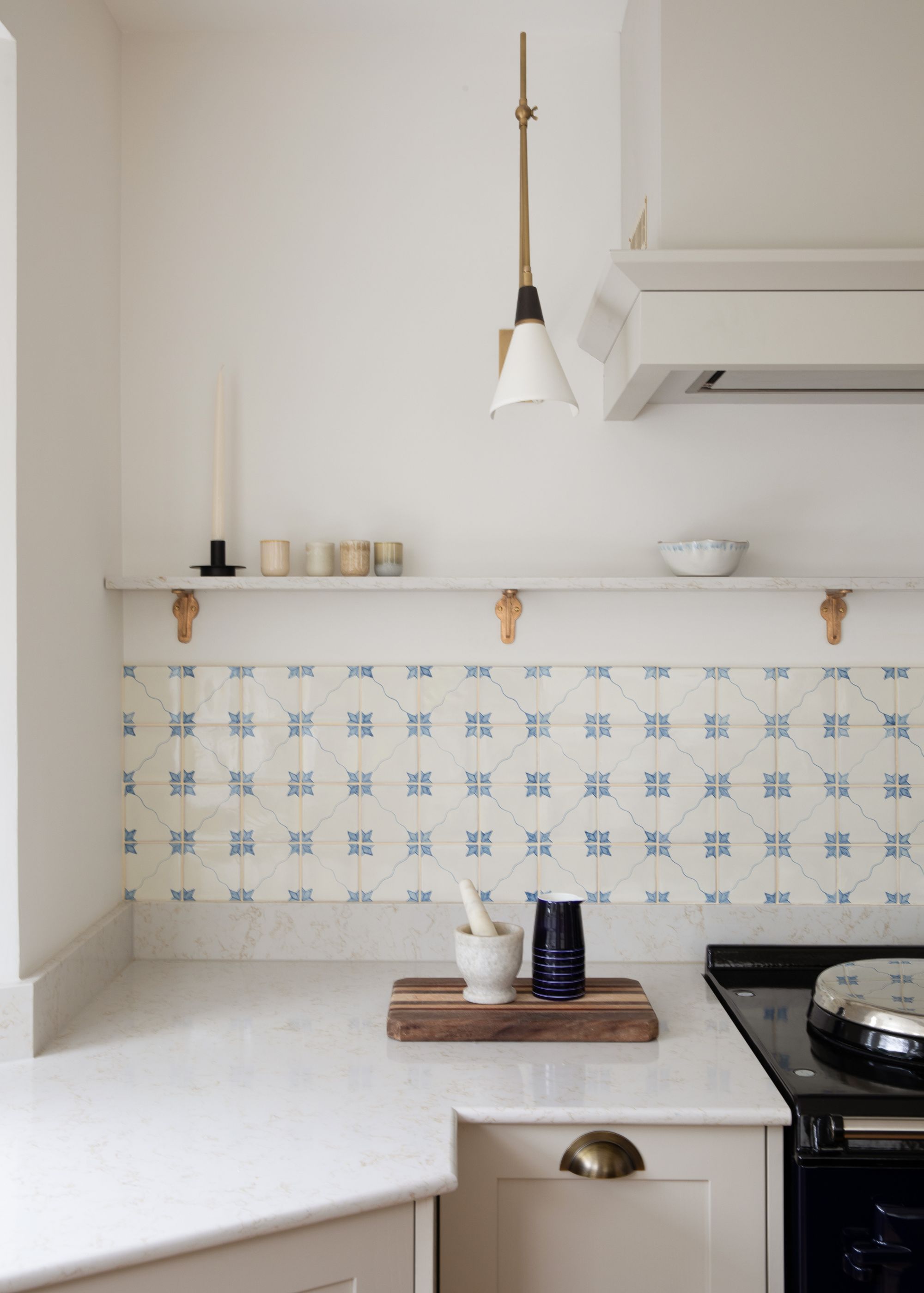 The corner of a kitchen with white walls, white countertops, and warm white cabinets. A pale blue and white tiled backsplash.