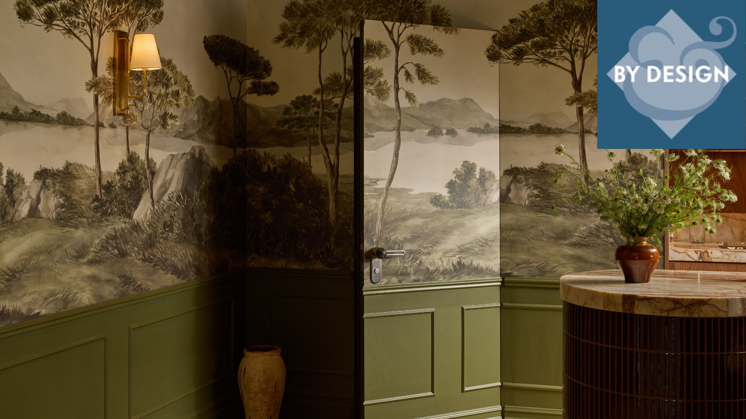 Close up of corner of room with green panelling and mural wallpaper across the top half of the wall, door into the room blends into the deisgn. 