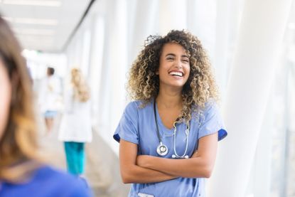 Blue Light Card: A confident young female healthcare professional laughs while standing in a hospital skybridge.