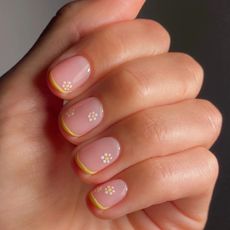 A yellow French tip manicure with mini yellow and white flowers