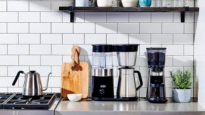 A stainless steel OXO 9-cup brewer on a kitchen counter against white subway tile wall. 