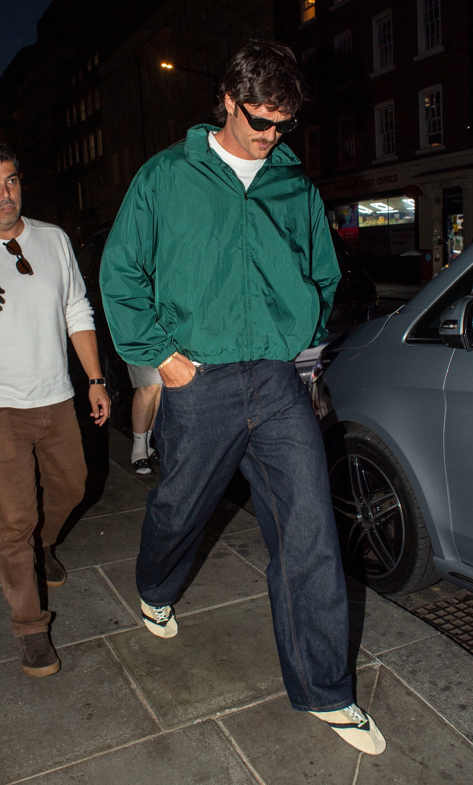 An image of Jacob Elordi wearing a green windbreaker with indigo jeans and Celine Flat Sneakers.