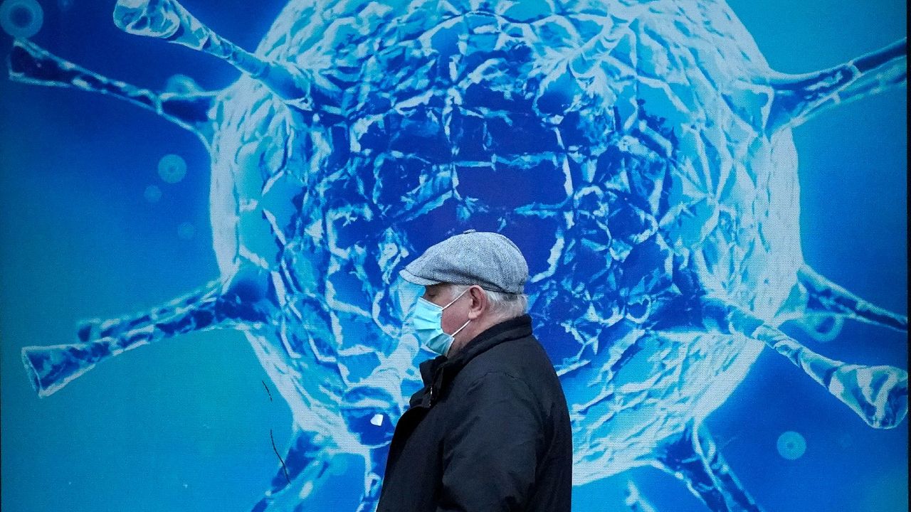 A man wearing a protective face mask walks past an illustration of a virus