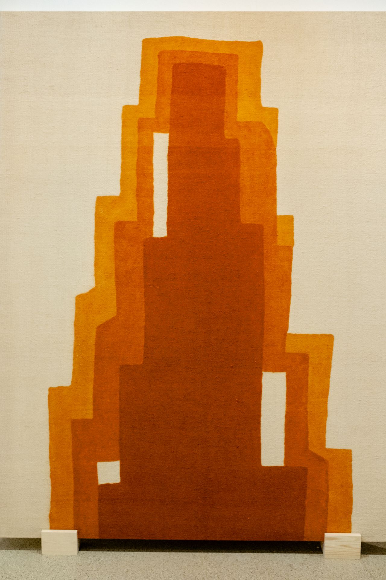 A textile installation features abstract, orange-tinted silhouettes that mimic the architecture of a stepped, triangular building.