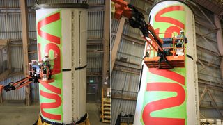 two views of a person on a crane painting the letters of 'nasa' on the side of a rocket, inside a warehouse