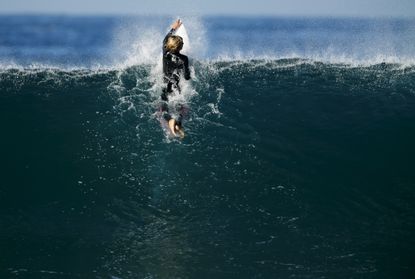 A surfer hangs on to his board as he navigates a breaking wave during high tide and high surf in Cardiff, California