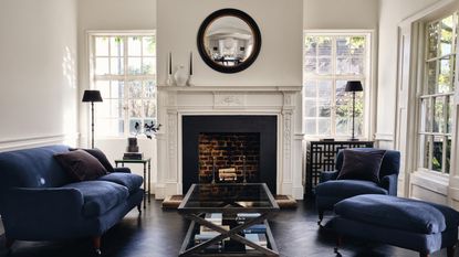 A mirror idea in a UK townhouse with black framed round mirror, fireplace and blue velvet sofas