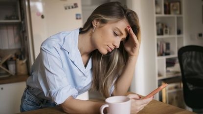 woman using her smartphone while drinking coffee in kitchen