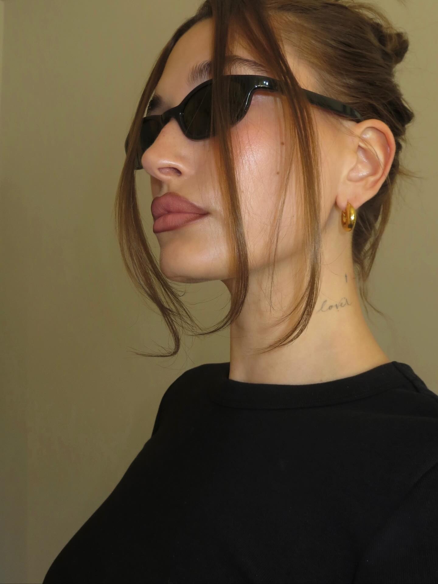 Hailey Bieber wearing a pair of black sunglasses with a chic updo hairstyle