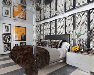 A black bedroom with a large screen behind a black headboard, with a geometric black and white pattern