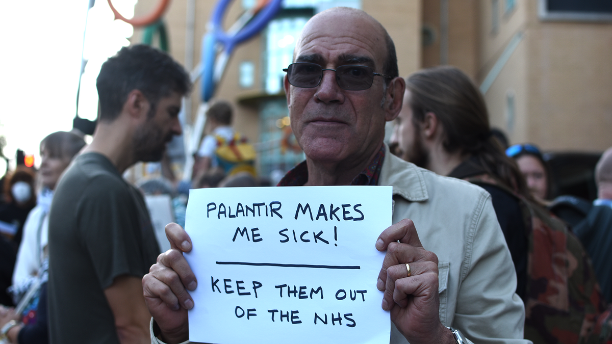 Man holding placards against Palantir in the NHS in front of the Bristol Royal Infirmary during a protest on October 1, 2026