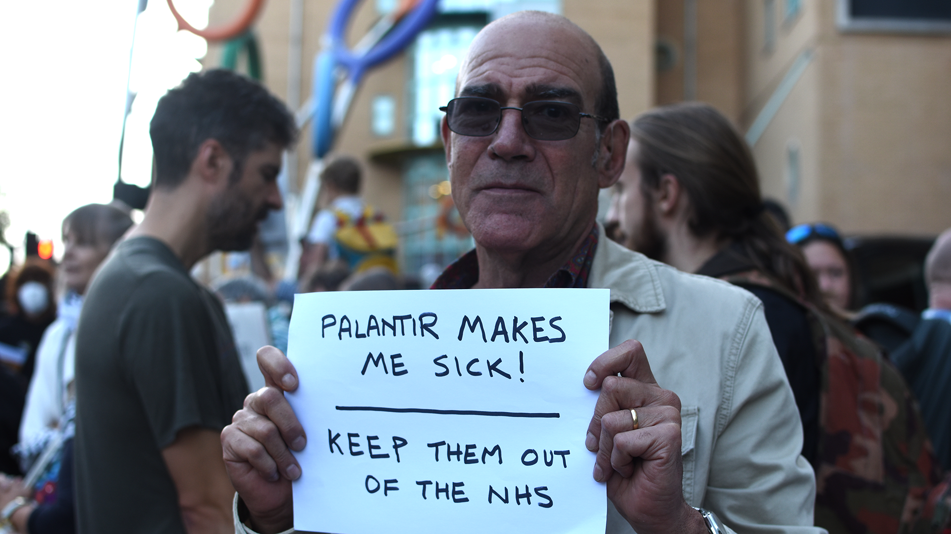Man holding placards against Palantir in the NHS in front of the Bristol Royal Infirmary during a protest on October 1, 2026