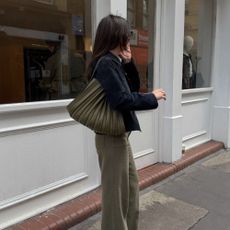 Woman wears black jacket, khaki jeans and khaki bag