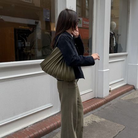 Woman wears black jacket, khaki jeans and khaki bag
