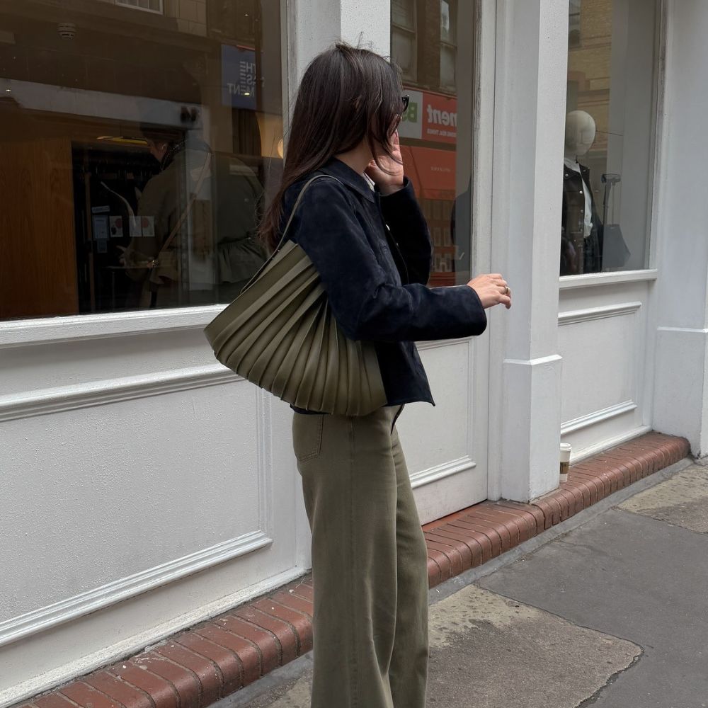 Woman wears black jacket, khaki jeans and khaki bag