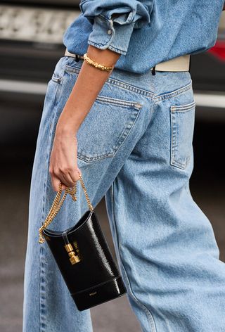 a close up street style photo of a woman wearing a denim outfit and carrying a cell phone crossbody purse