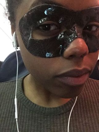 Woman taking a selfie wearing headphones and a 'Phantom of the Opera' looking face mask