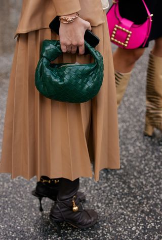 a closeup photo of a woman wearing a brown pleated skirt with brown heels and a bottega veneta bag from a second-hand site