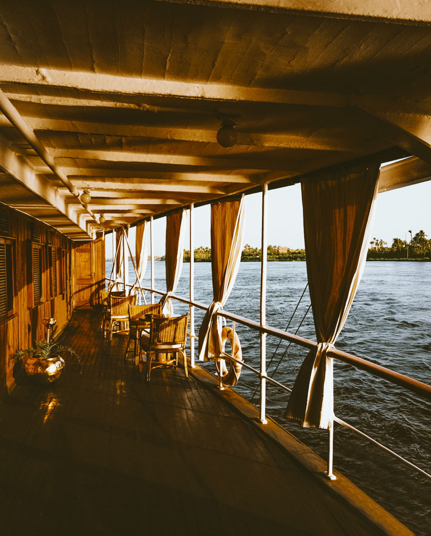 A view from onboard SS Sudan, showing wicker chairs arranged on a deck with the Nile flowing past in the background