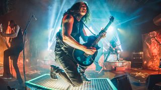 Alex Skolnick kneels down to play his ESP singlecut onstage, blue lights behind him