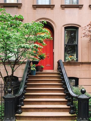 Steps leading up to a townhouse painted pink with a red front door