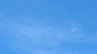 A translucent moon against a bright blue sky taken with the Google Pixel 8a.