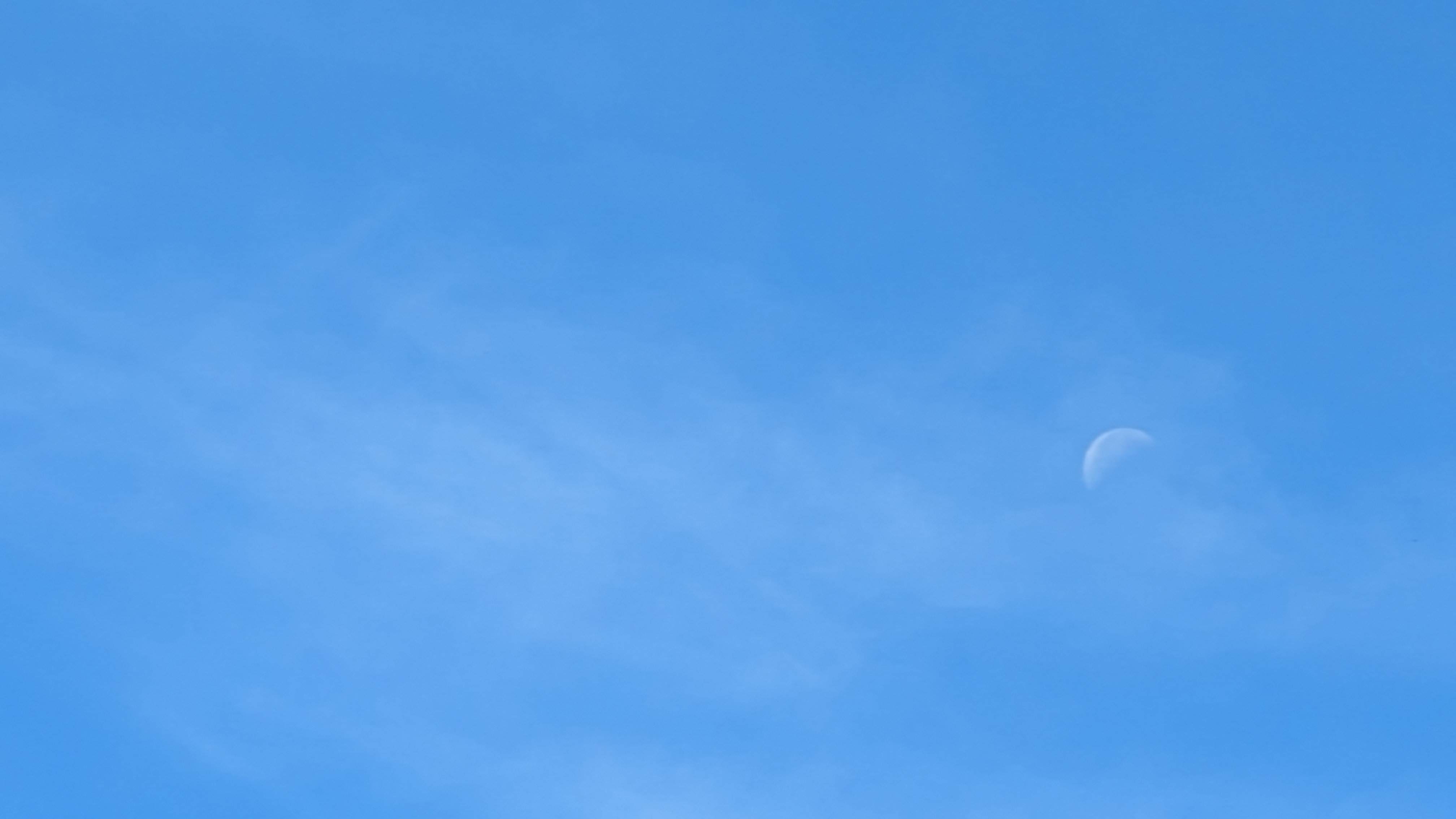 A translucent moon against a bright blue sky taken with the Google Pixel 8a.