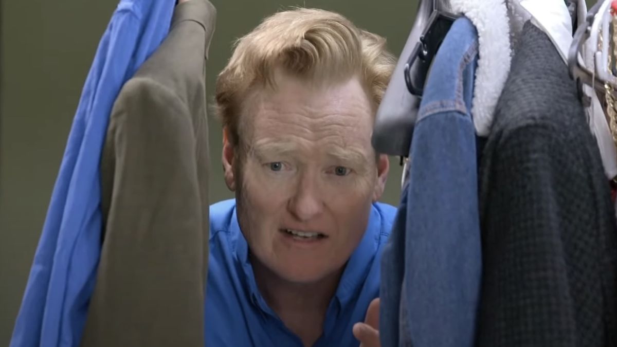 Screenshot of Conan O&#039;Brien peeking through hanging clothes in Thailand in Conan O&#039;Brien Must Go