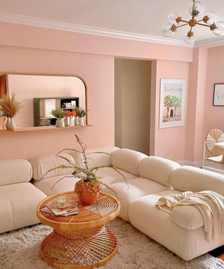 A pink living room with a white couch, rattan table, and curved mirror on the wall