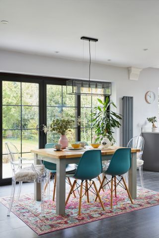 Dining area of open-plan kitchen-diner with table and chairs on a patterned pink rug, with Crittall-style French doors leading out to patio