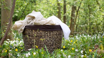 A full wicker laundry basket sat on the grass near to some yellow flowers