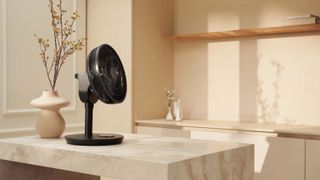 A black tabletop fan on a marble kitchen counter