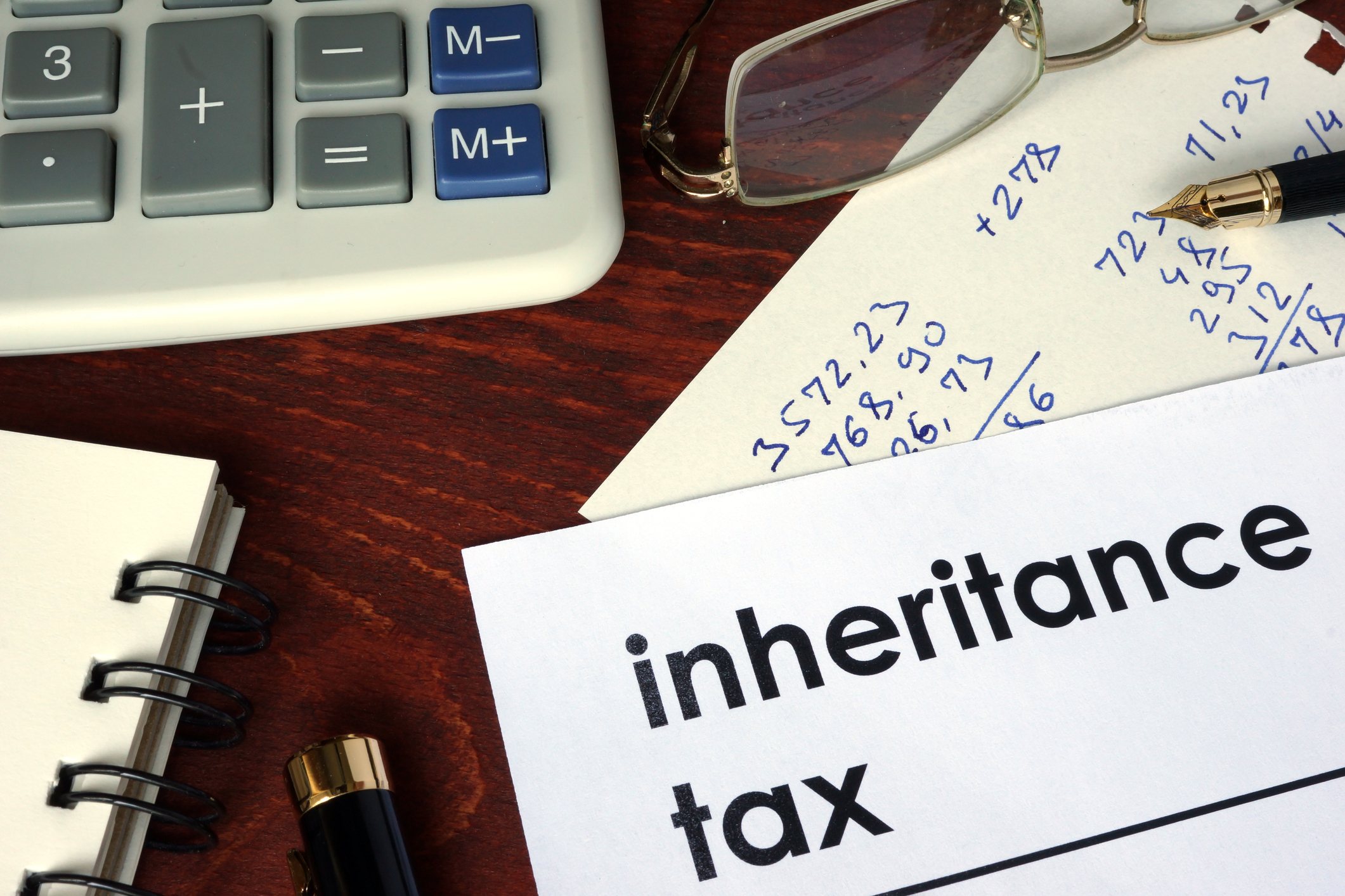 "inheritance tax" printed on paper with pen, glasses, calculator, and other desk supplies