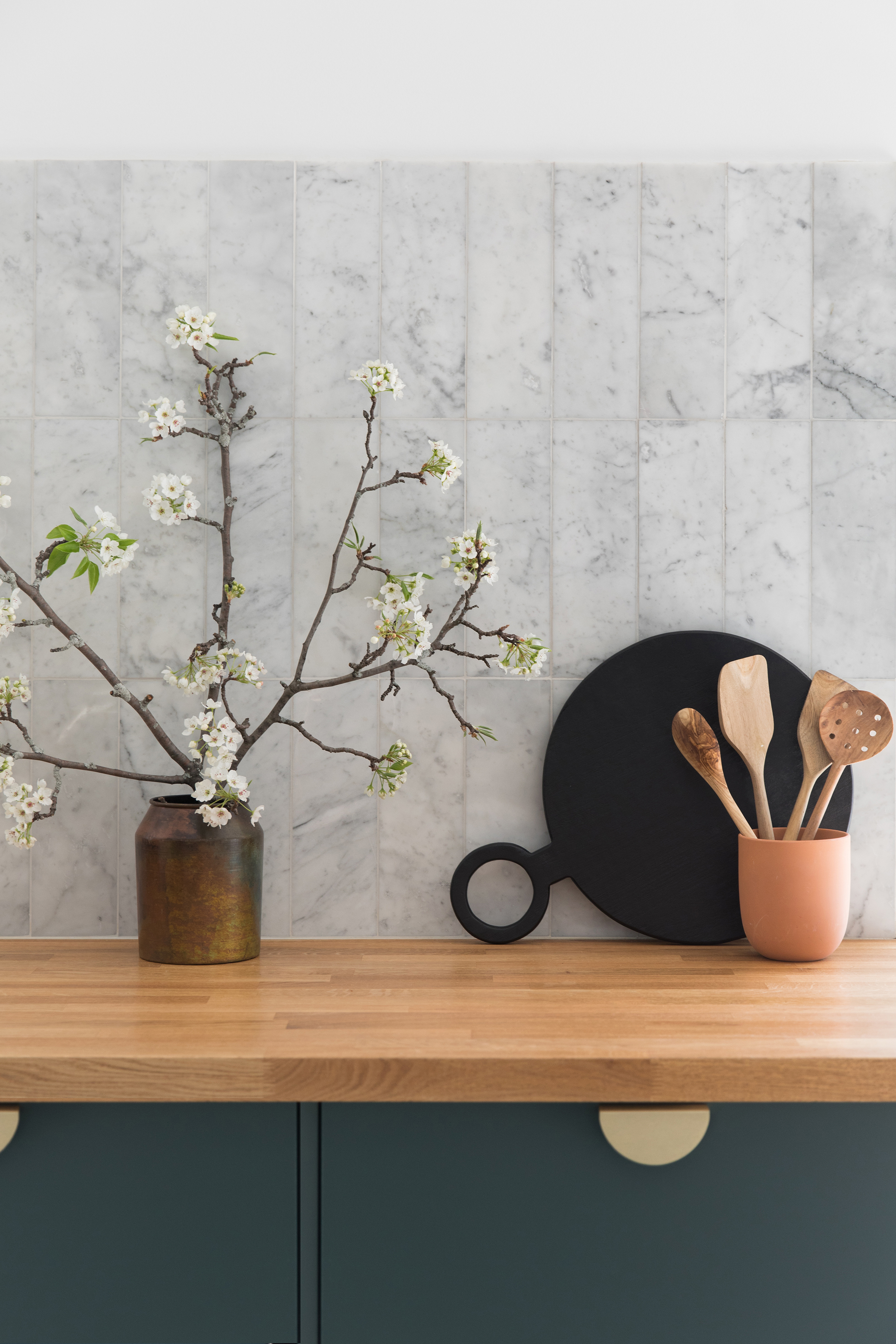 A light oak wooden countertop with a vase and a plant and on the right are utensils with cookware