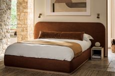 brown velvet upholstered bed in a modern bedroom with stone walls