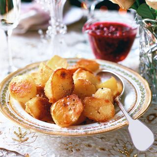 Roast potatoes in serving dish next to cranberry sauce