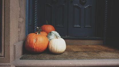 Two orange pumpkins and a small white on a porch outside
