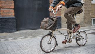 Male cyclist riding a Brompton folding bike with Barbour bags mounted