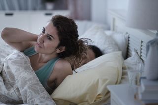 A woman in a bed struggling to sleep next to sleeping partner